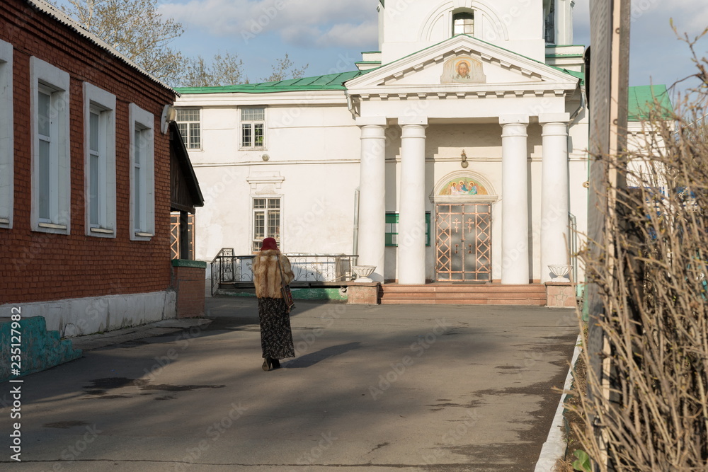 Woman goes to the Holy Trinity Cathedral (1836) of the Krasnoyarsk city, in the spring afternoon.