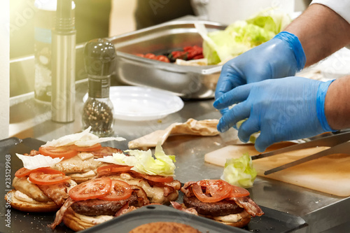 The process of cooking hamburger. Chef at the kitchen table decorates burger ingredients. Vegetables and cheese and homemade sauces.