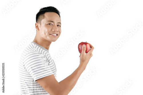 Waist-up portrait of young handsome Asian man holding red apple and smiling at camera happily against white background