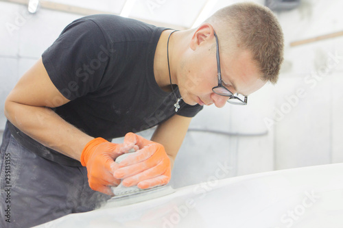 cute cheerful guy with glasses polishes the hood of a car pneumatic polishing machine