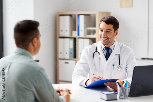 medicine, healthcare and people concept - doctor with clipboard talking to male patient at medical office in hospital