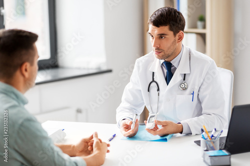 medicine, healthcare and diabetes concept - doctor with glucometer and insulin pen device talking to male patient at medical office in hospital photo