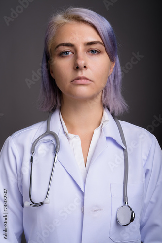 Young beautiful woman doctor with short colorful hair against gr