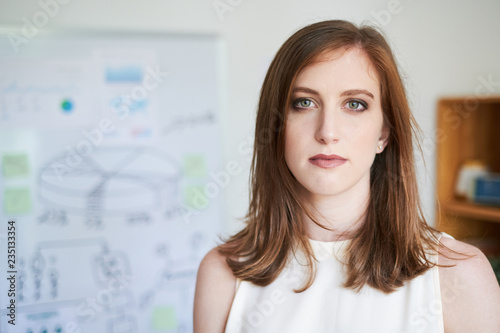 Young Caucasian businesswoman in white shirt looking at camera standing indoors