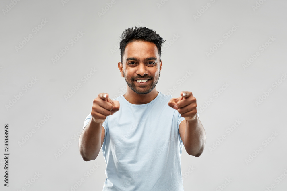 Naklejka premium choice and people concept - smiling young indian man pointing fingers at you over grey background