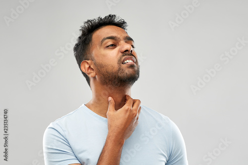 health problem and people concept - unhealthy indian man suffering from neck pain or sore throat over grey background photo