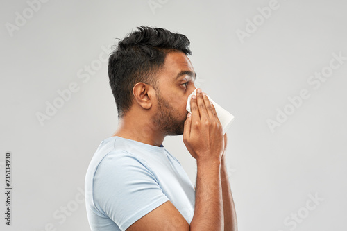 health problem, rhinitis and allergy concept - unhealthy indian man with paper napkin blowing nose over grey background