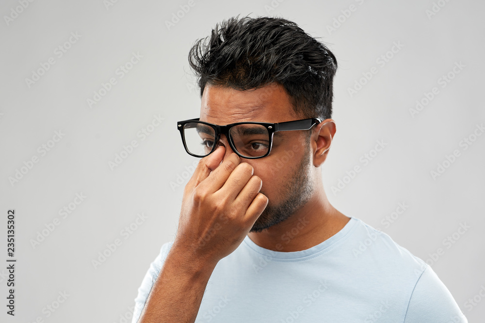 people, vision and overwork concept - tired indian man in glasses rubbing nose bridge over grey background people, vision and overwork concept - tired indian man in glasses rubbing nose bridge over grey background