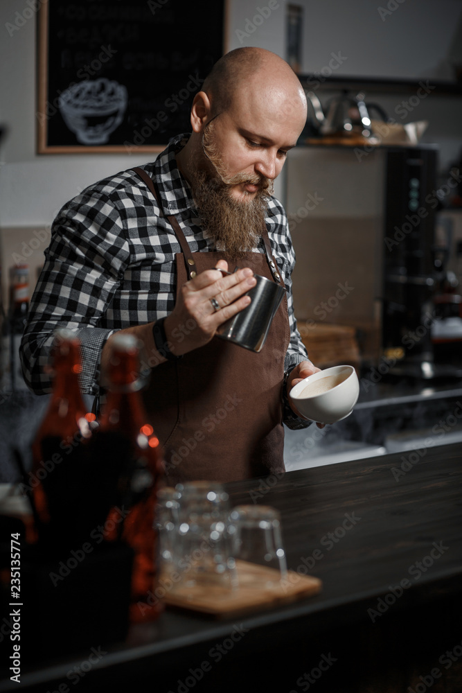 Brutal young barista in an apron makes coffee at the bar in a modern cafe Brutal young barista in an apron makes coffee at the bar in a modern cafe