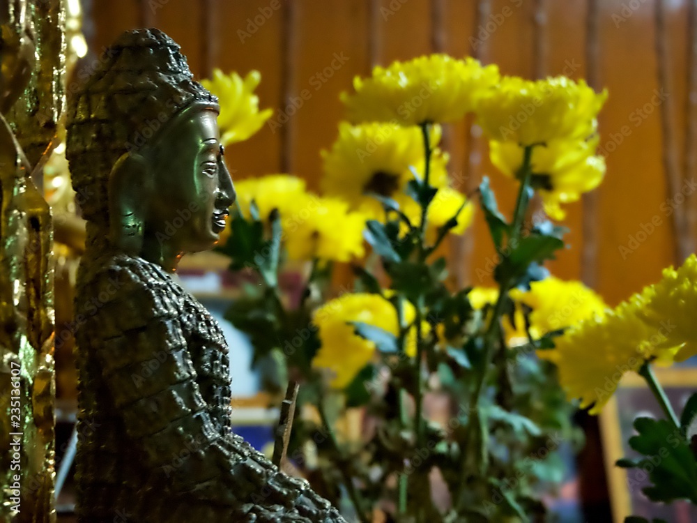 A side portrait of ancient lord buddha statue with yellow flower