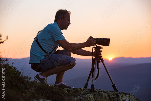 Portrait of man with camera and tripod filming sunset above mountain. Traveler Taking pictures from the top of mountain. Beautiful view of pink sky, Norway, Kongsberg photo