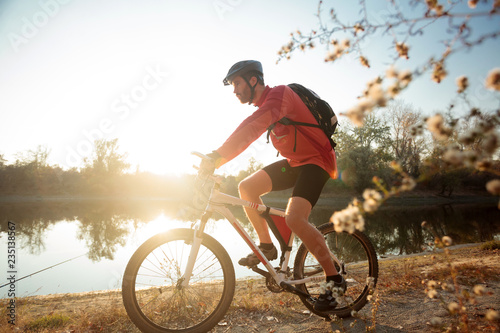 Canvas Print Determined young bearded man in long sleeve jersey riding a mountain bike by the lake or river