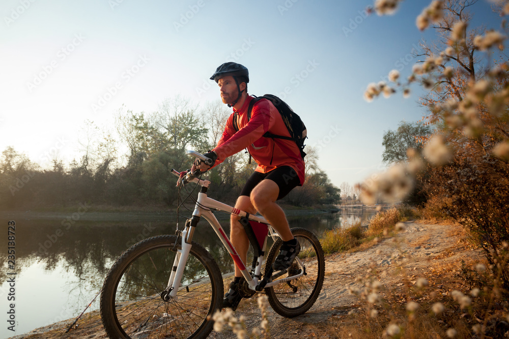 Determined young bearded man in long sleeve jersey riding a mountain bike by the lake or river