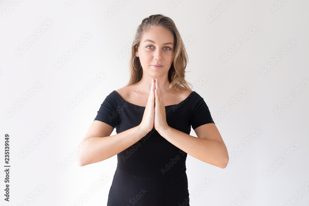 Positive pretty Caucasian girl pressing hands in mudra gesture. Young white woman in black dress finding happiness. Peace and harmony concept Positive pretty Caucasian girl pressing hands in mudra gesture. Young white woman in black dress finding happiness. Peace and harmony concept