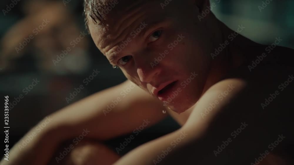 Exhausted male athlete is resting after training, looking at camera, close-up. Drops of water is draining from his face, workout in gym