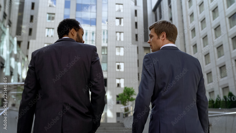 Coworkers discussing business plan walking together near building, cooperation