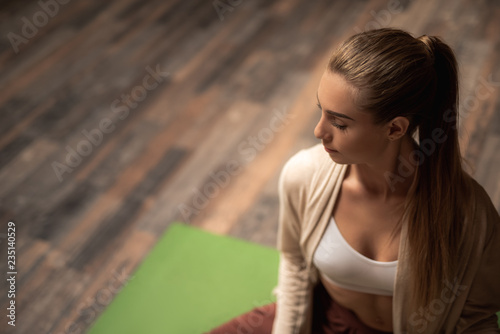 Close up of calm young woman sitting on the yoga mat and feeling relaxed during the yoga practice