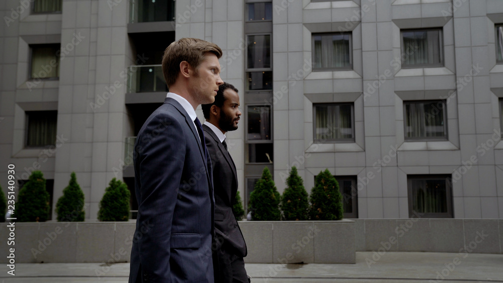 Two men in business suits going near office center, business district in city Two men in business suits going near office center, business district in city