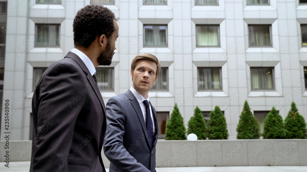 Multiracial coworkers walking near business center, discussing issues at break Multiracial coworkers walking near business center, discussing issues at break