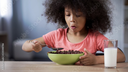 фотографія Cute little girl eating chocolate cornflakes for breakfast, risk of diabetes