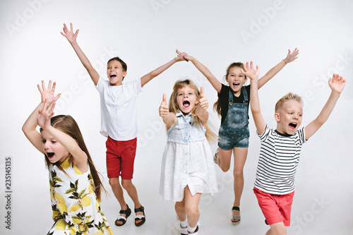 Group of fashion cute preschooler kids friends running together and looking at camera on a white studio background. The friendship, fashion, summer concept. Space for text.