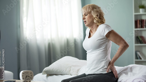 Fotografia Aged woman suffering from low back pain, sitting on bed, spinal disk herniation