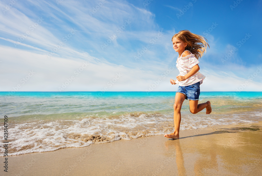 Adorable girl running along sandy beach in summer