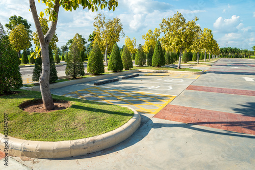 Fototapeta Naklejka Na Ścianę i Meble -  Empty space in city park outdoor concrete parking lot area with blue sky in summer season. Green nature gardening in car parking lot. Friendly environmental and transportation concept.