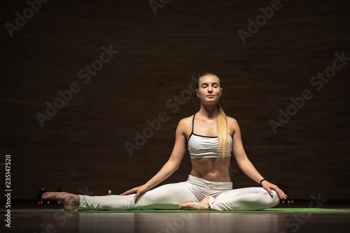 Peaceful slim lady slightly smiling while sitting on the yoga mat with straight back and meditating with closed eyes