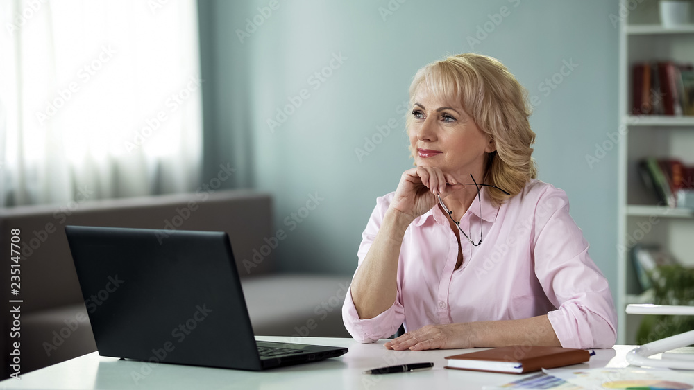 Mature female writer thinking of new series of adventure books in front laptop Mature female writer thinking of new series of adventure books in front laptop
