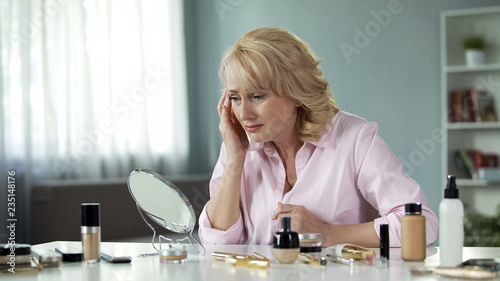 Tableau sur toile Mature lady looking with disgust at her sagging skin and wrinkles, aging process