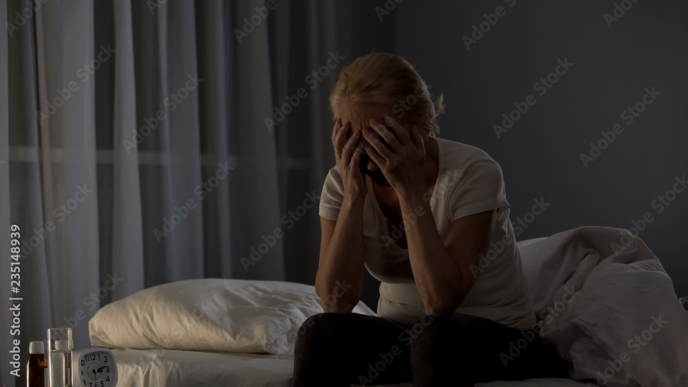 Sad blond lady sitting on bed night, covering face with hands, health disorder Sad blond lady sitting on bed night, covering face with hands, health disorder