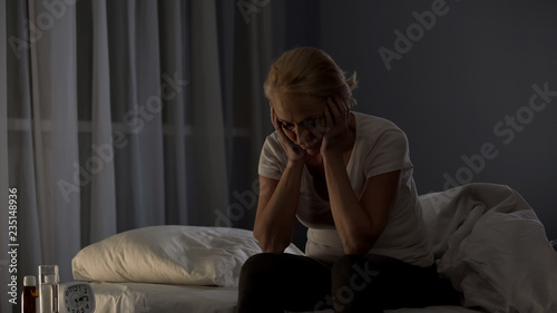 Canvas Print Tired middle-aged woman sitting on bed at night, insomnia disease, problem