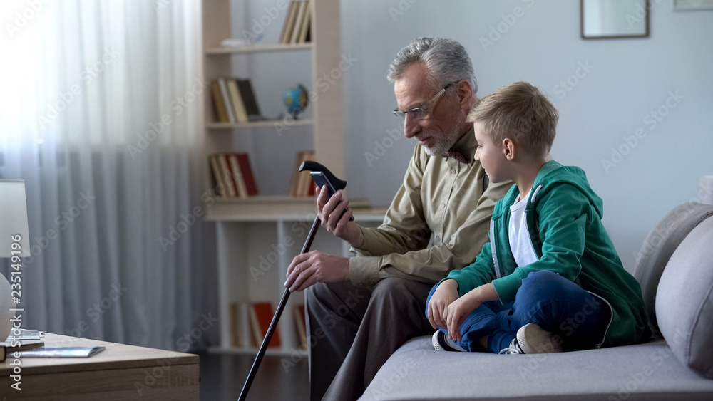 Grandfather holding phone, boy helping him to acquaintance with new technologies