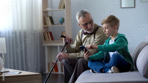 Boy explaining to old man how to use cell phone, simple technologies for old man © motortion