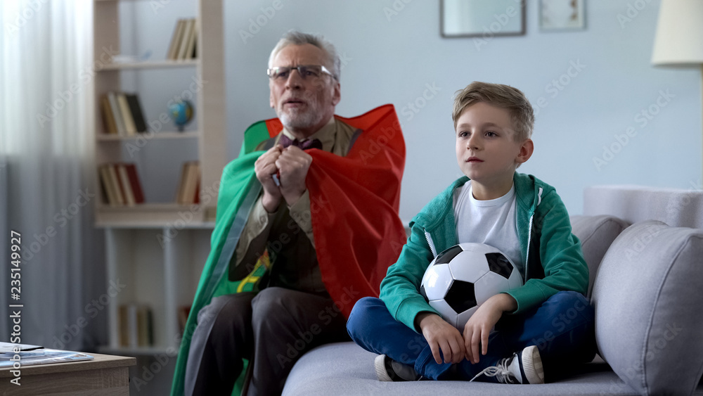 Grandpa wrapped in Portuguese flag watching soccer with boy, worrying about game