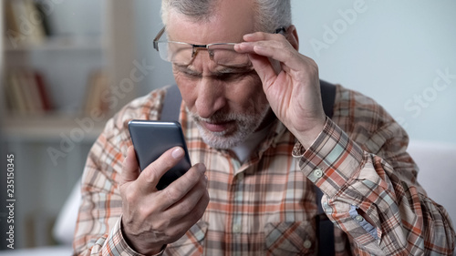 Bewildered old man looking at cellphone, new technology complicated for elderly