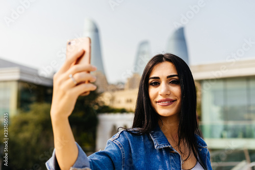beautiful black-haired girl travels through Azerbaijan, makes selfie on the background of modern buildings