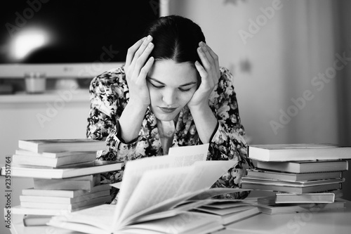 Fotografie A young woman sits in front of a pile of papers and a computer holding her head