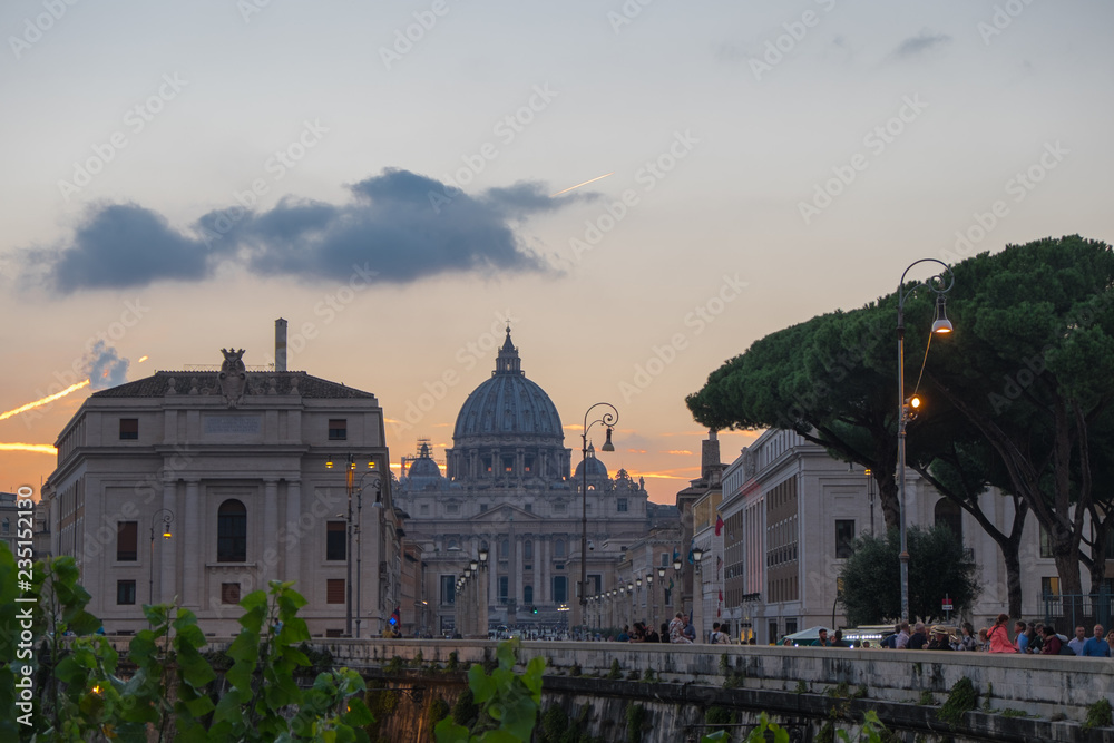 The view of Saint Peter's Dome and Vatica in dusk, with crowded streets and traces of aircrafts in the sky