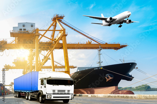 Container truck on road with container ship during unloaded in the commercial harbor with airplane flying in the sky. delivery cargo transportation concept