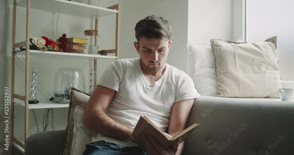 Seriously man in the morning have a personal time reading a book sitting on the sofa , watching on the window , cozy atmosphere. 4k Seriously man in the morning have a personal time reading a book sitting on the sofa , watching on the window , cozy atmosphere. 4k