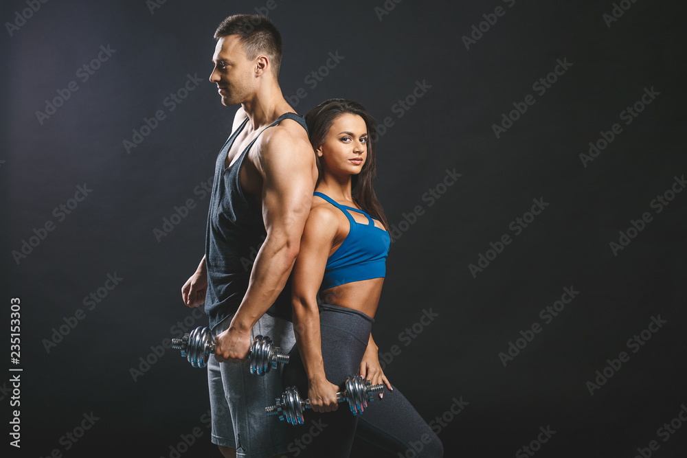 Obraz premium Sporty young sexy couple isolated over black background with dumbbells.