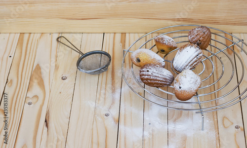 French madeleine cookies powdered sugar, strainer on natural wooden light-colored background. Chocolate chip cookies. Copy space. Flat lay.