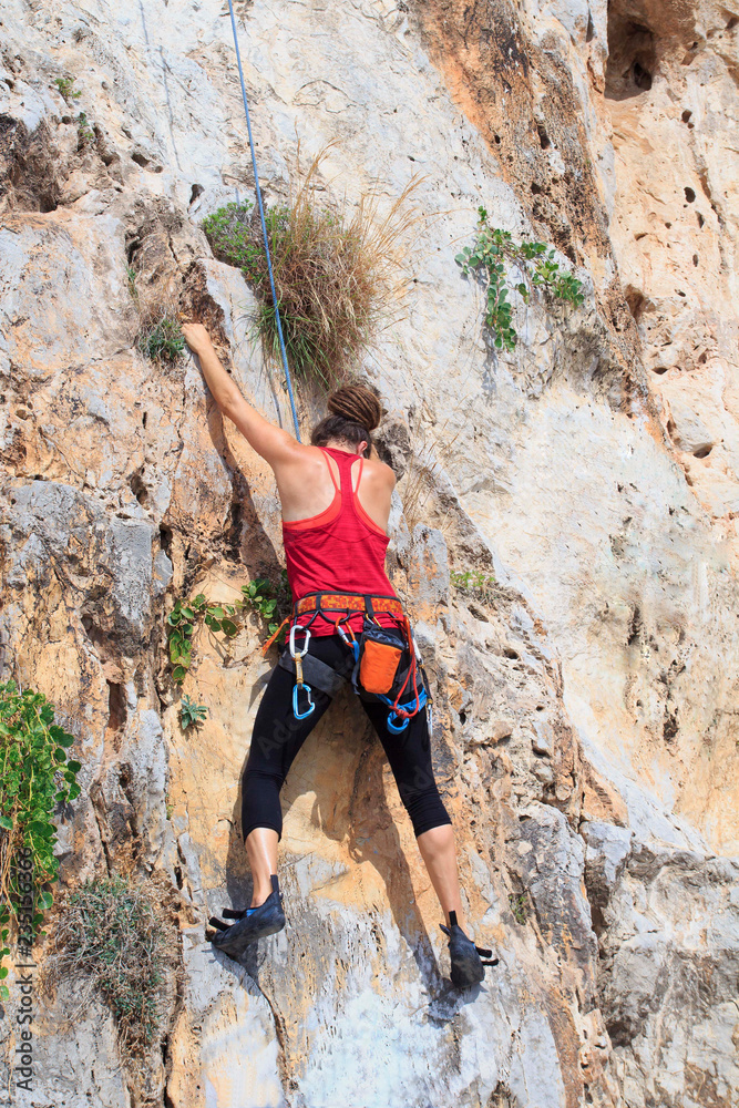 A young woman with a rope engaged in the sports of rock climbing on the rock.