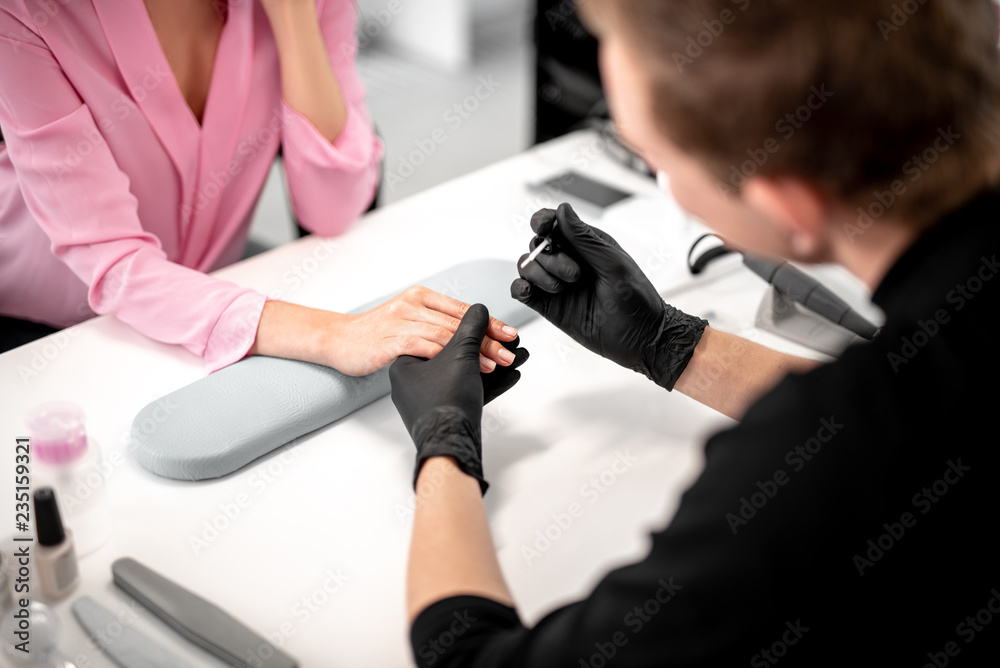 Professional manicurist in black gloves holding nail color and touching the hand of his client while working Professional manicurist in black gloves holding nail color and touching the hand of his client while working