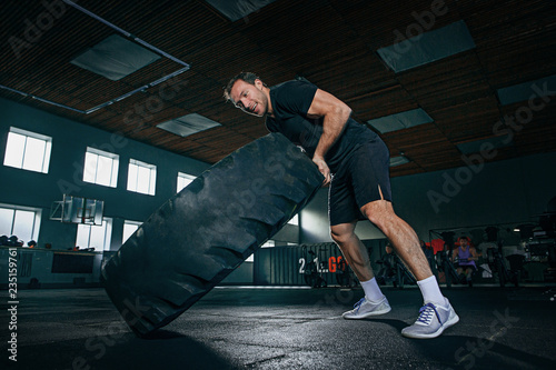 Shirtless young fit man flipping heavy tire with battle rope at gym. The exercise, fitness, sport, workout, athlete, power, training, bodybuilding concept
