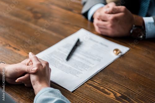 partial view of lawyer and client sitting at table with divorce decree and wedding rings photo