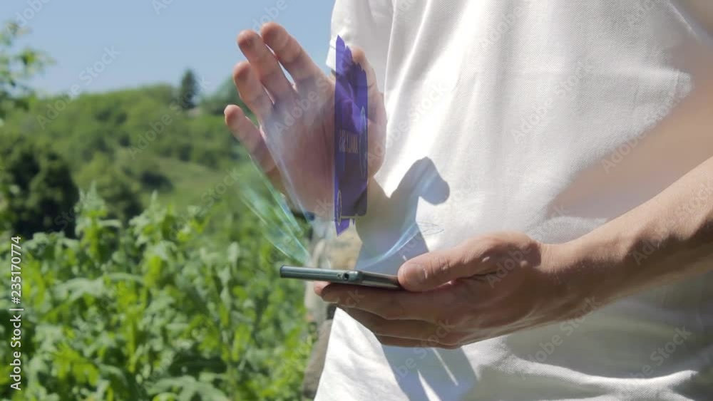 Man shows concept hologram Analysis on his phone. Person in white t-shirt with future technology holographic screen and green nature background Man shows concept hologram Analysis on his phone. Person in white t-shirt with future technology holographic screen and green nature background