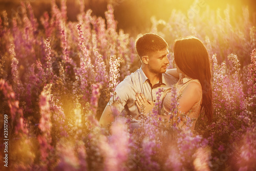 beautiful young couple hugging in the field with flowers in the sun, the concept of a love relationship